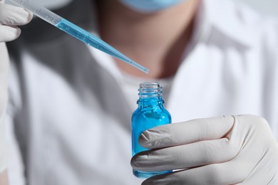 Scientist dripping liquid from pipette into glass bottle, closeup