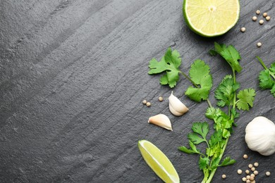 Photo of Fresh coriander leaves, dried seeds, garlic and lime on black textured table, flat lay. Space for text