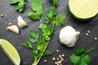 Fresh coriander leaves, dried seeds, garlic and lime on black textured table, flat lay