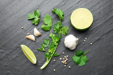 Photo of Fresh coriander leaves, dried seeds, garlic and lime on black textured table, flat lay