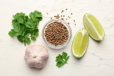 Fresh coriander leaves, dried seeds, garlic and lime wedges on light textured table, flat lay