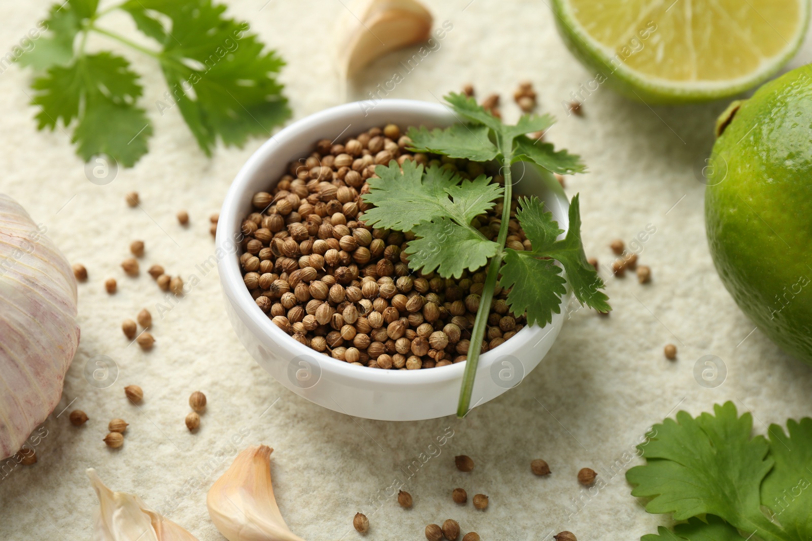 Photo of Fresh coriander leaves, dried seeds, garlic and limes on light textured table, closeup