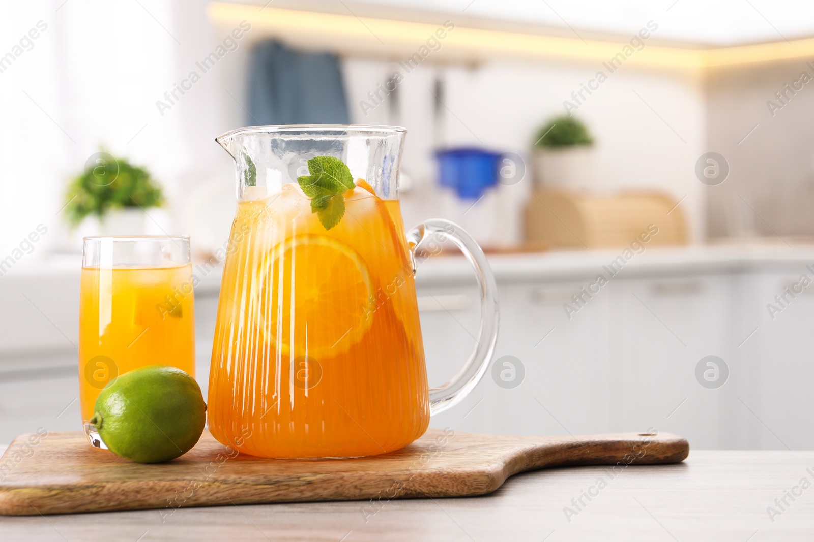 Photo of Tasty lemonade with orange in jug, glass and lime on wooden table in kitchen, space for text