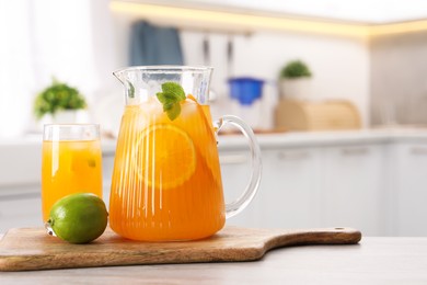 Tasty lemonade with orange in jug, glass and lime on wooden table in kitchen, space for text