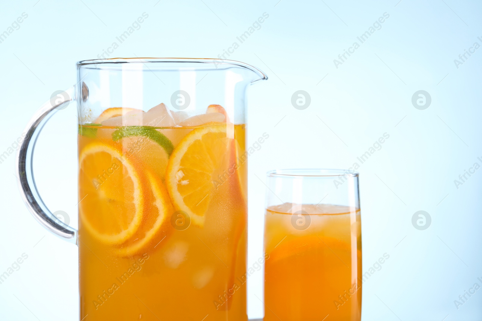 Photo of Freshly made lemonade in jug and glass against light blue background