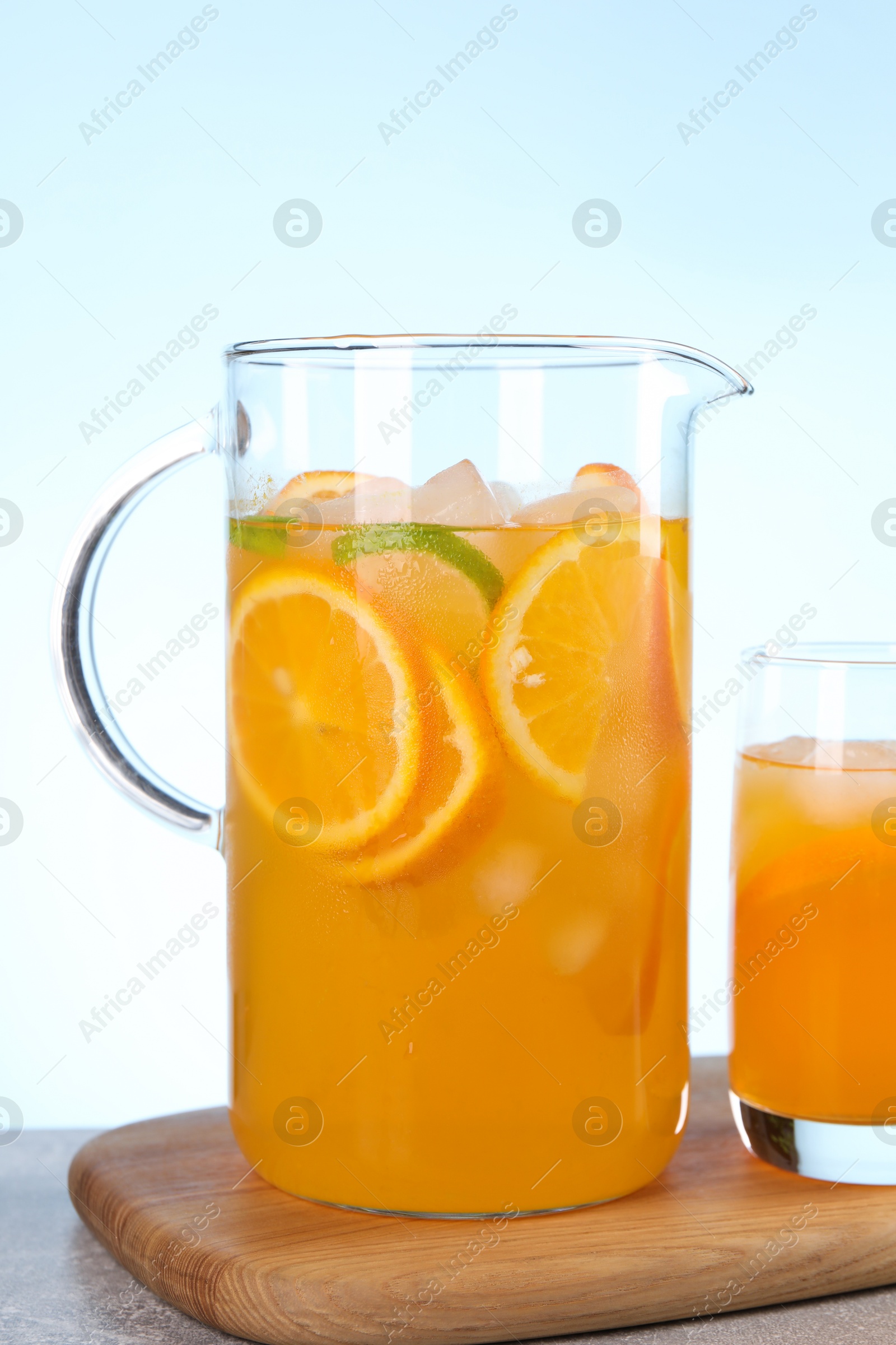 Photo of Freshly made lemonade in jug and glass on table against light blue background