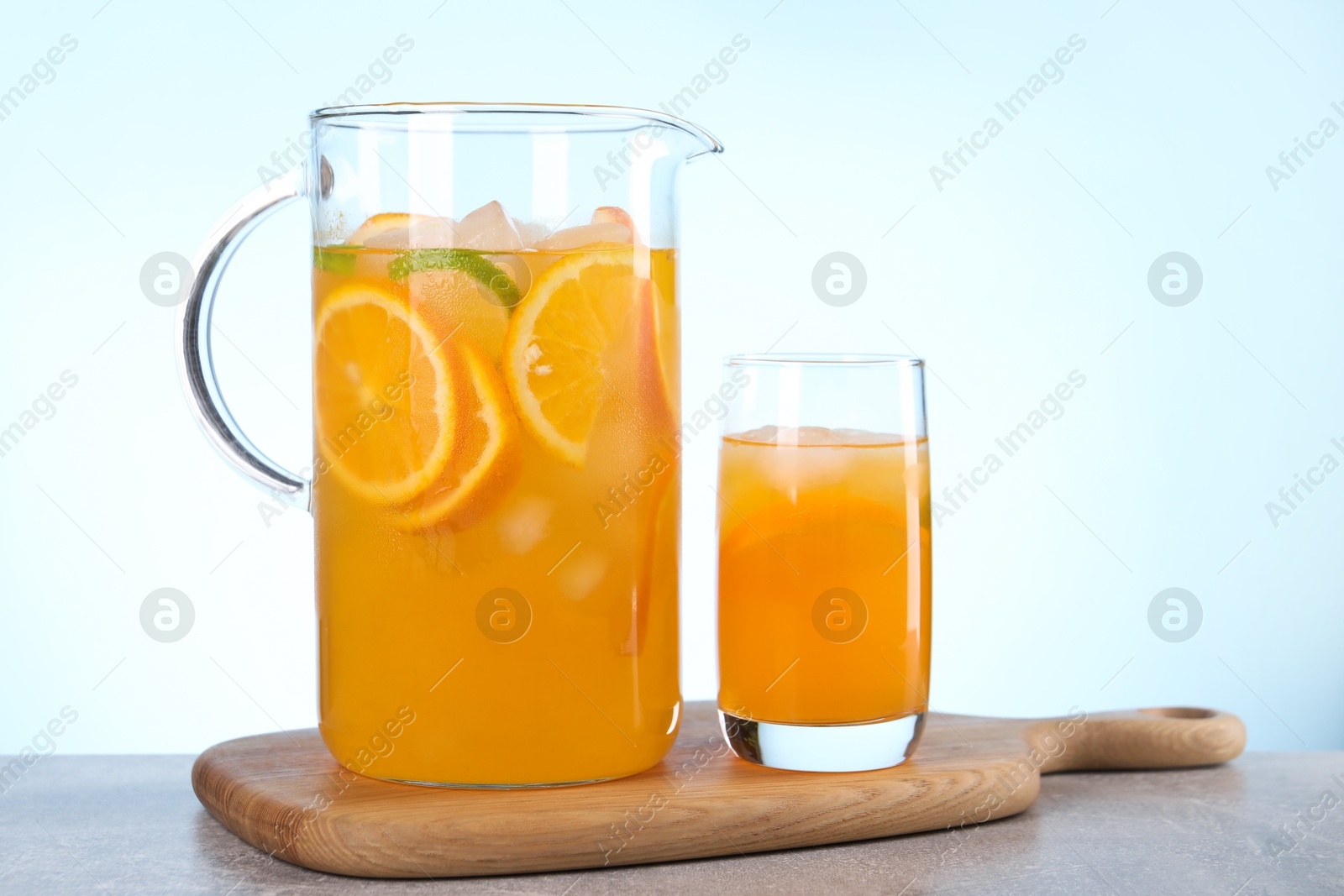 Photo of Freshly made lemonade in jug and glass on grey table against light blue background