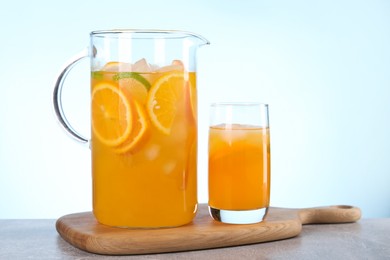 Freshly made lemonade in jug and glass on grey table against light blue background