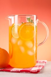 Photo of Freshly made lemonade in jug and orange on light wooden table