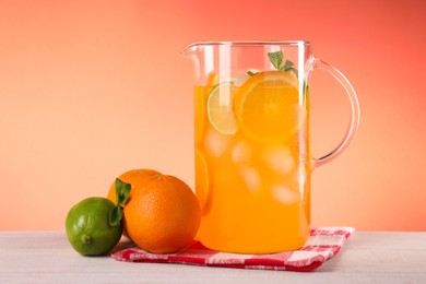 Freshly made lemonade in jug and citrus fruits on light wooden table