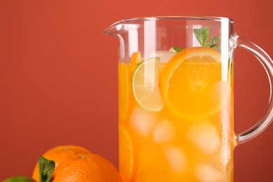 Photo of Freshly made lemonade in jug and citrus fruits against coral background