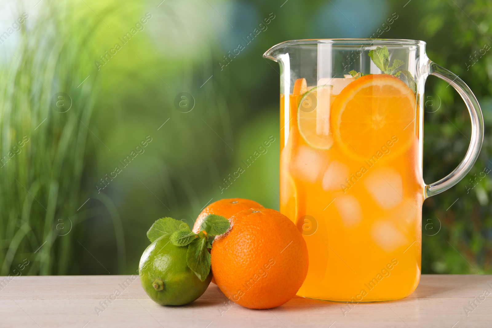 Photo of Freshly made lemonade in jug and citrus fruits on light wooden table outdoors, space for text