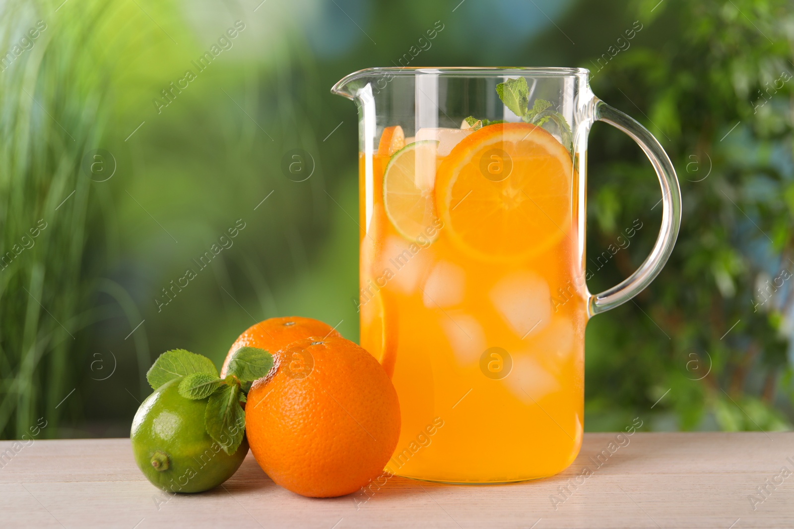 Photo of Freshly made lemonade in jug and citrus fruits on light wooden table outdoors