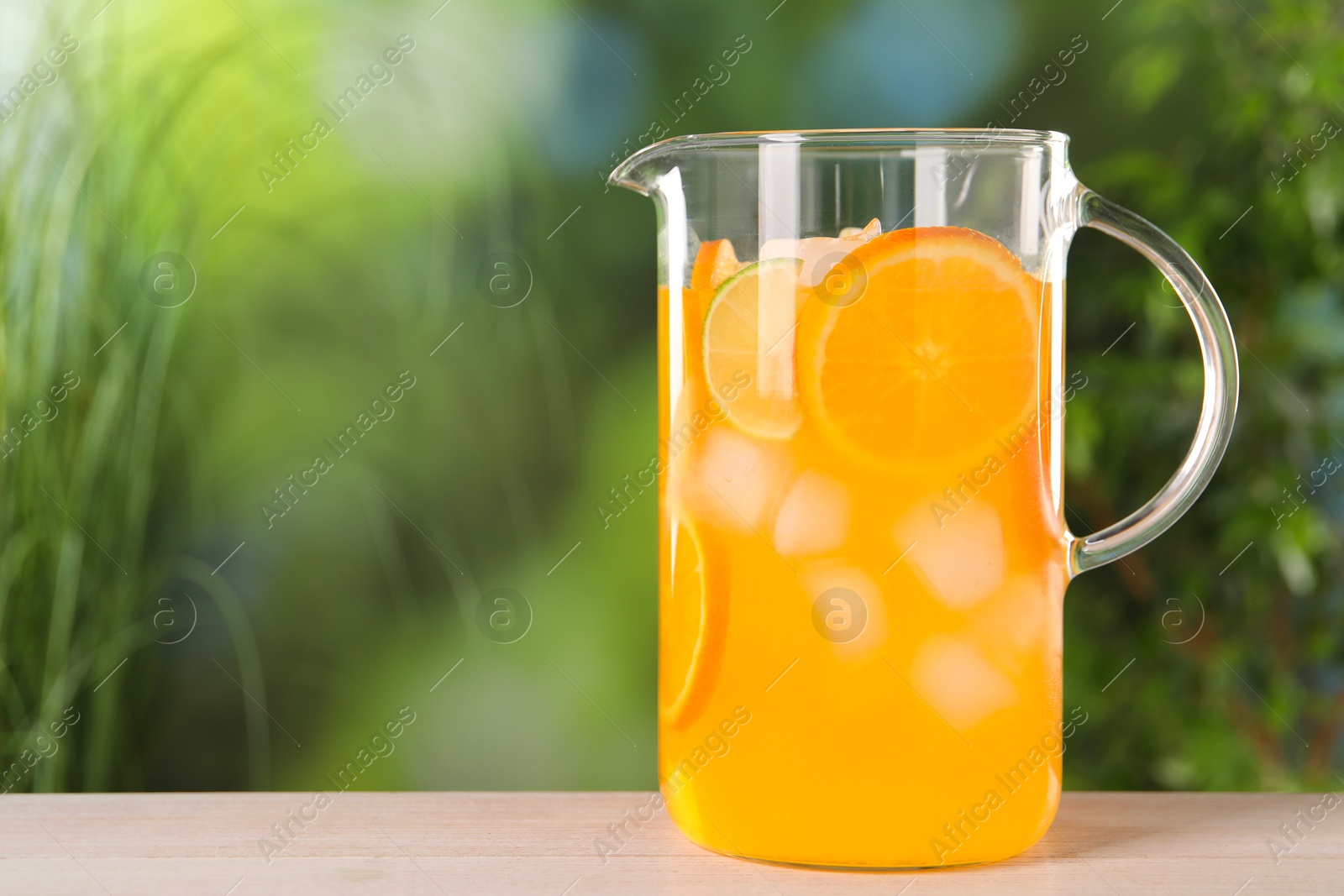 Photo of Freshly made lemonade in jug on light wooden table outdoors, space for text