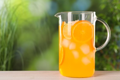 Photo of Freshly made lemonade in jug on light wooden table outdoors, space for text