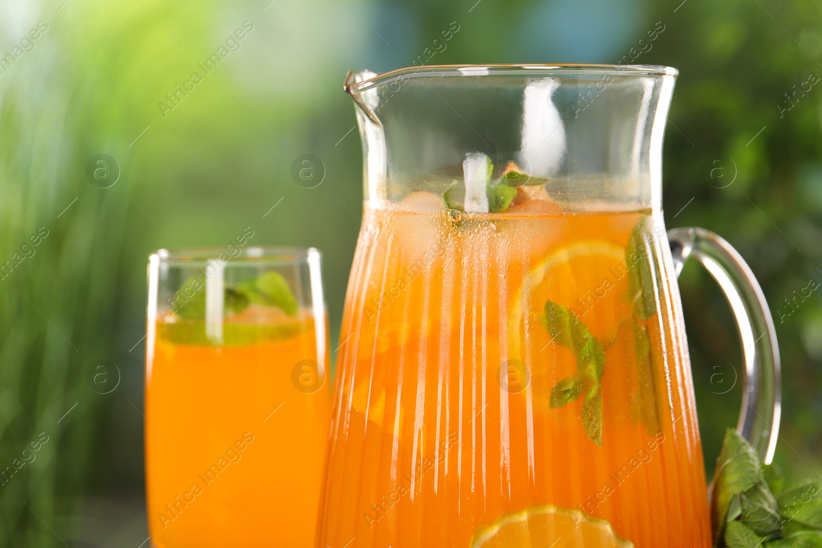 Photo of Freshly made lemonade in jug and glass outdoors