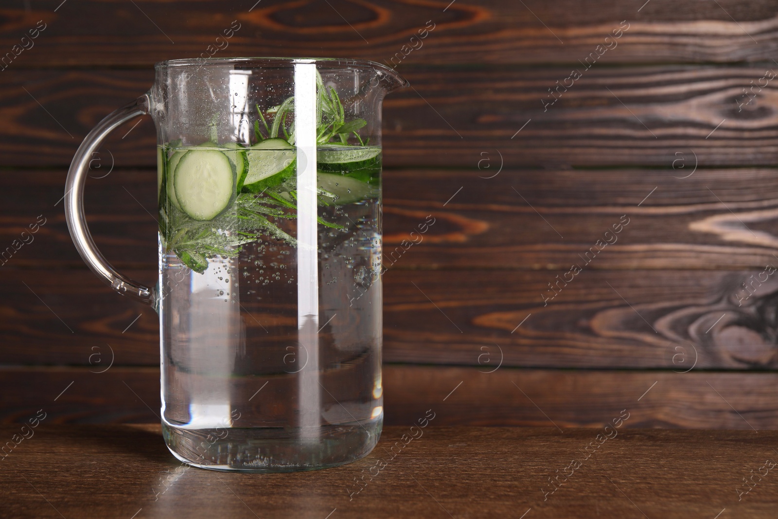 Photo of Refreshing cucumber water with rosemary in jug on wooden table. Space for text