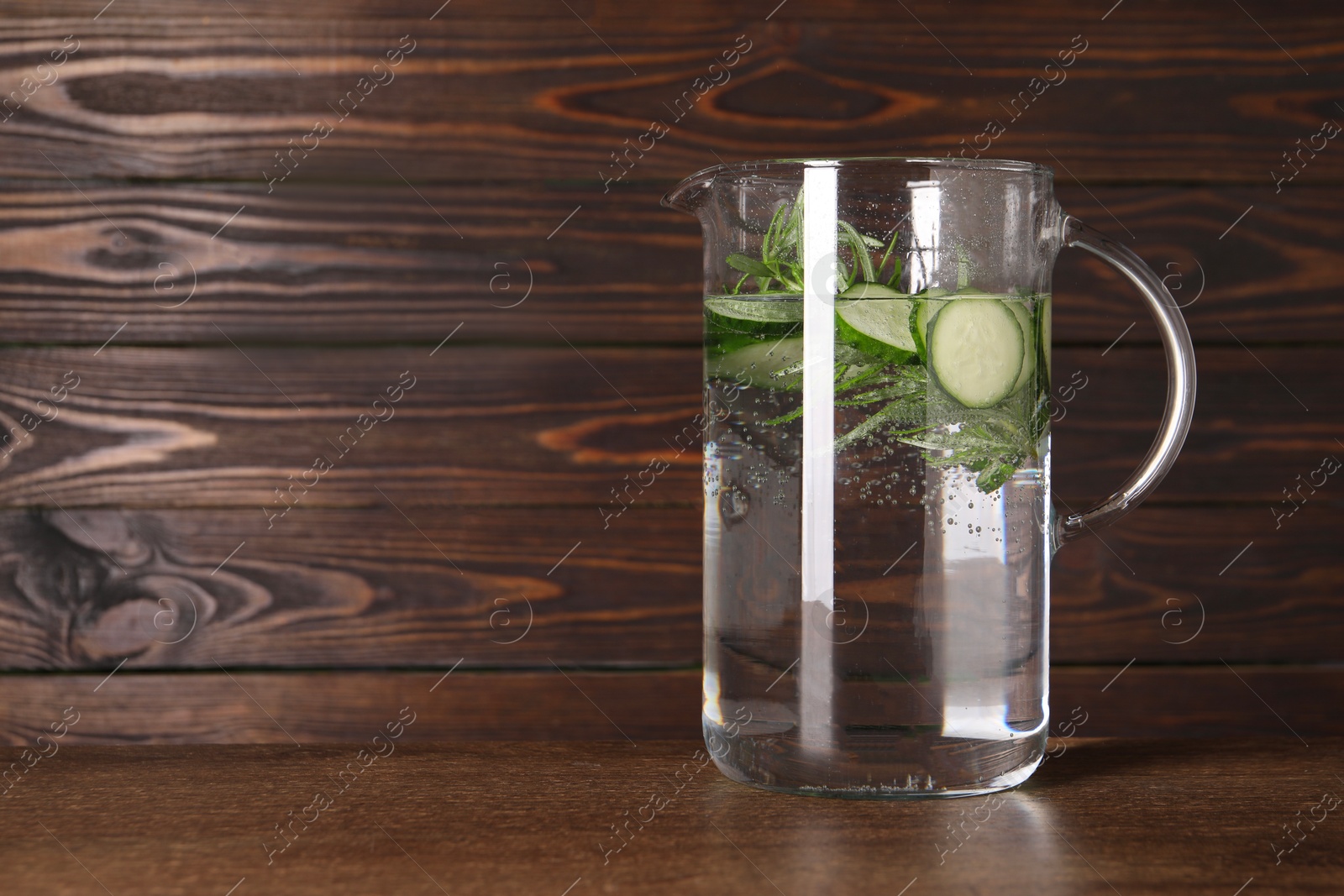 Photo of Refreshing cucumber water with rosemary in jug on wooden table. Space for text