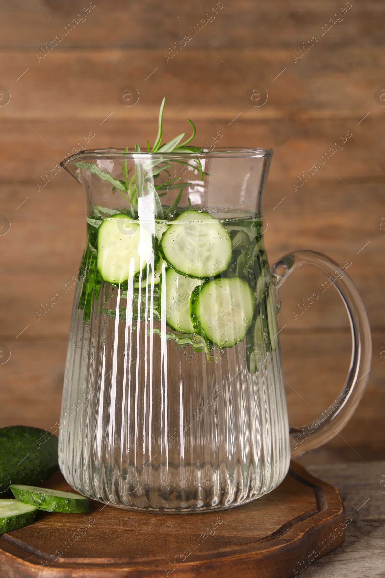 Photo of Refreshing cucumber water with rosemary in jug on wooden table