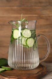 Refreshing cucumber water with rosemary in jug on wooden table