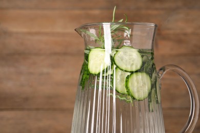 Refreshing cucumber water with rosemary in jug on blurred background, closeup. Space for text