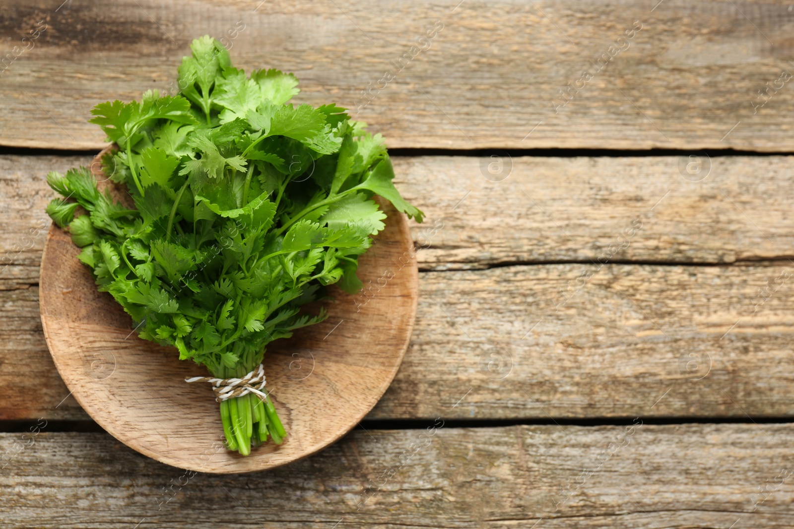 Photo of Bunch of fresh coriander on wooden table, top view. Space for text