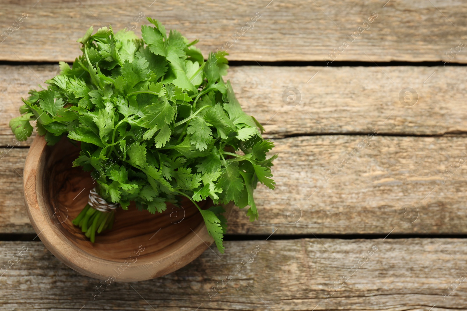 Photo of Bunch of fresh coriander in bowl on wooden table, top view. Space for text