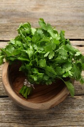 Bunch of fresh coriander in bowl on wooden table, top view