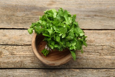 Photo of Bunch of fresh coriander in bowl on wooden table, top view