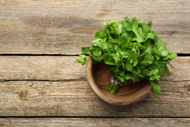 Bunch of fresh coriander in bowl on wooden table, top view. Space for text