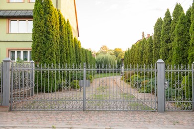 Photo of House and trees behind beautiful iron fence outdoors