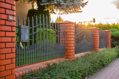 Photo of Bushes and beautiful brick fence with iron railing outdoors