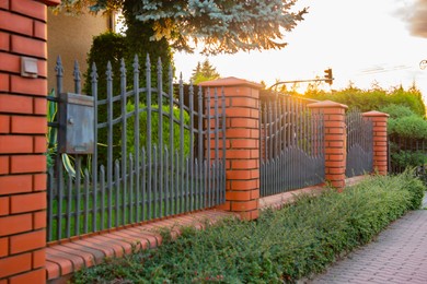 Photo of Bushes and beautiful brick fence with iron railing outdoors