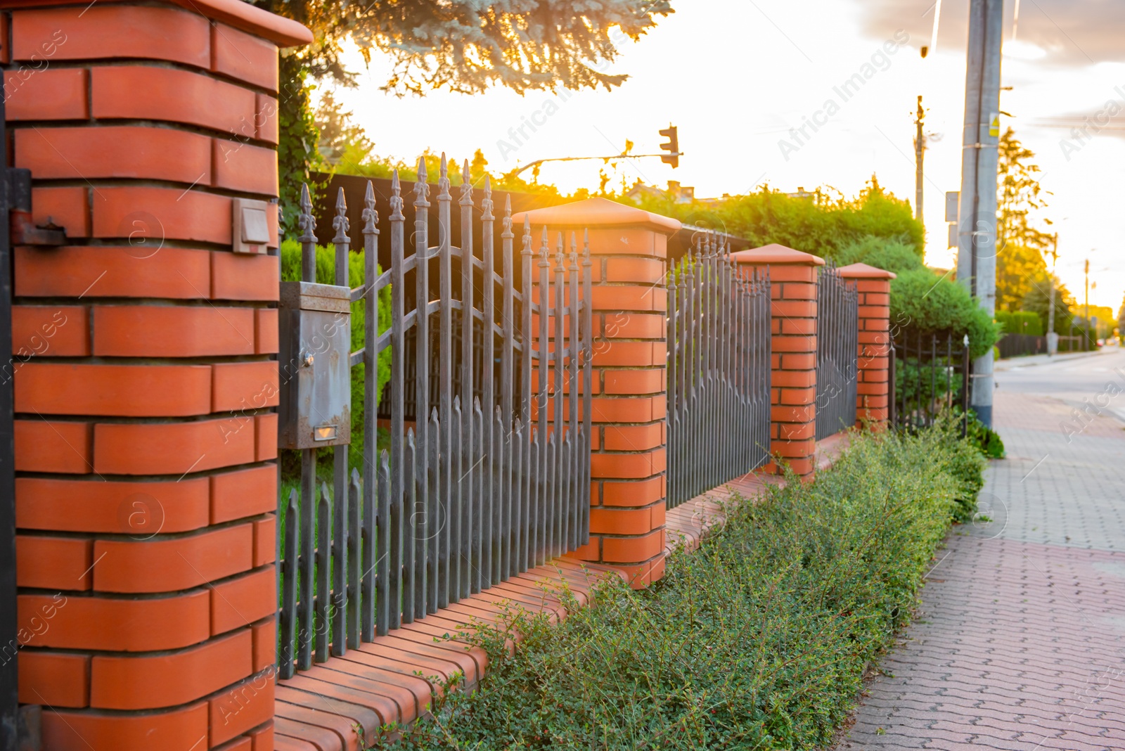 Photo of Bushes and beautiful brick fence with iron railing outdoors