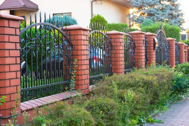 Photo of Bushes and beautiful brick fence with iron railing outdoors