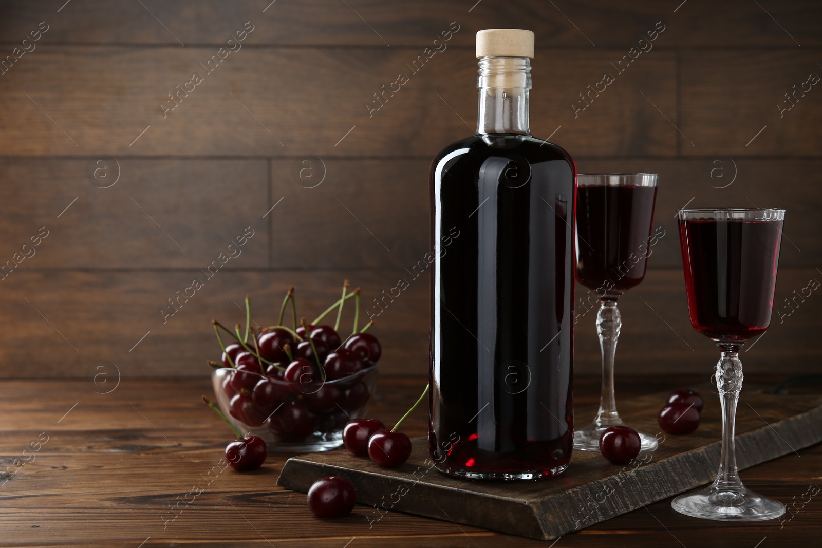 Photo of Delicious cherry liqueur and berries on wooden table. Space for text