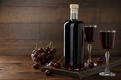 Delicious cherry liqueur and berries on wooden table. Space for text