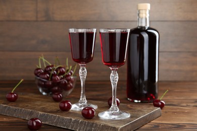 Photo of Delicious cherry liqueur and berries on wooden table