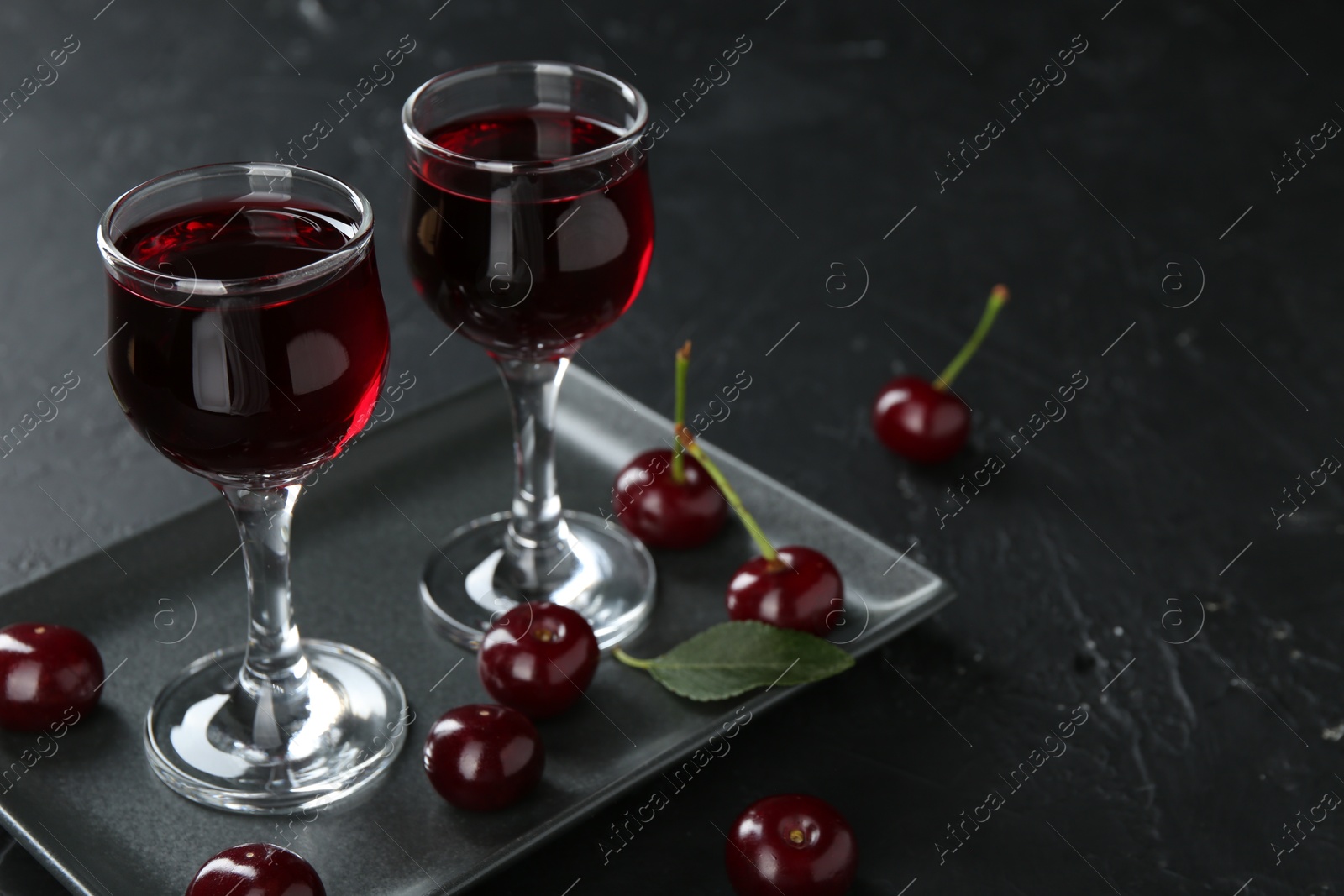 Photo of Delicious cherry liqueur in glasses and berries on black table, closeup. Space for text