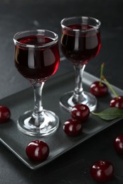 Photo of Delicious cherry liqueur in glasses and berries on black table, closeup