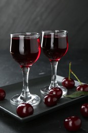 Delicious cherry liqueur in glasses and berries on black table, closeup