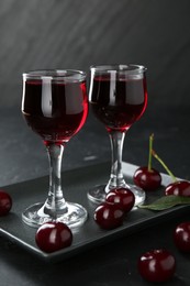 Photo of Delicious cherry liqueur in glasses and berries on black table, closeup