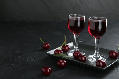 Photo of Delicious cherry liqueur in glasses and berries on black table. Space for text