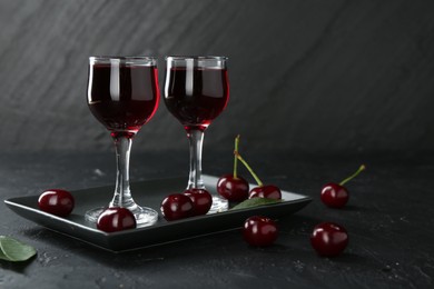 Photo of Delicious cherry liqueur in glasses and berries on black table