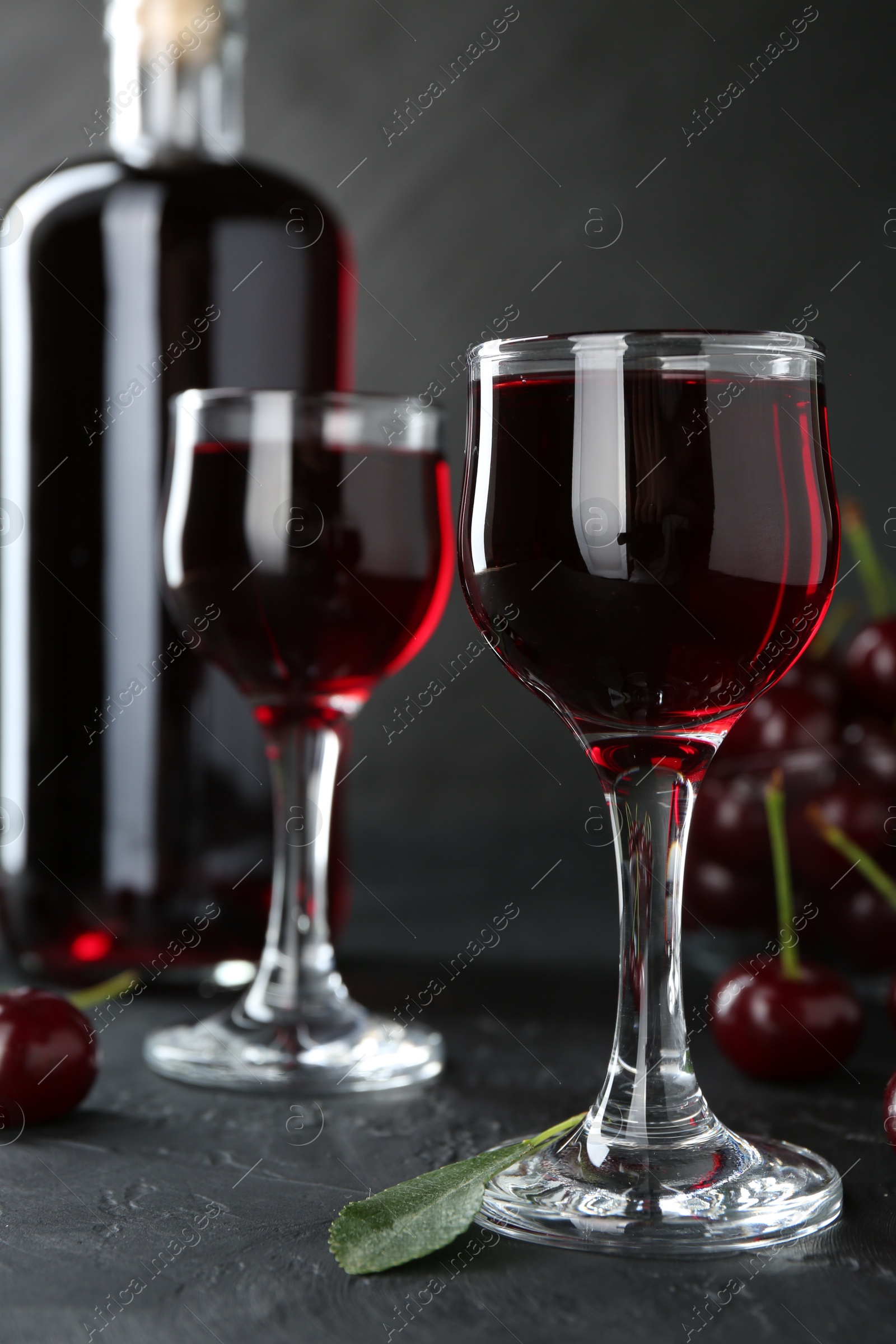 Photo of Delicious cherry liqueur and berries on black table, closeup