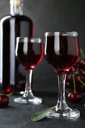 Delicious cherry liqueur and berries on black table, closeup