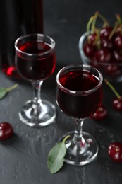 Delicious cherry liqueur in glasses and berries on black table, closeup