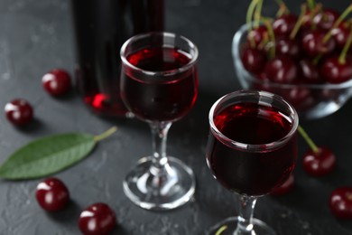 Delicious cherry liqueur in glasses and berries on black table, closeup