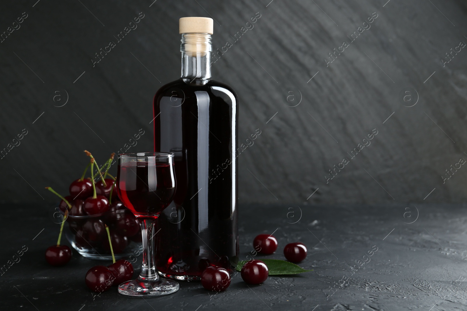 Photo of Delicious cherry liqueur and berries on black table. Space for text
