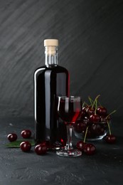 Photo of Delicious cherry liqueur and berries on black table